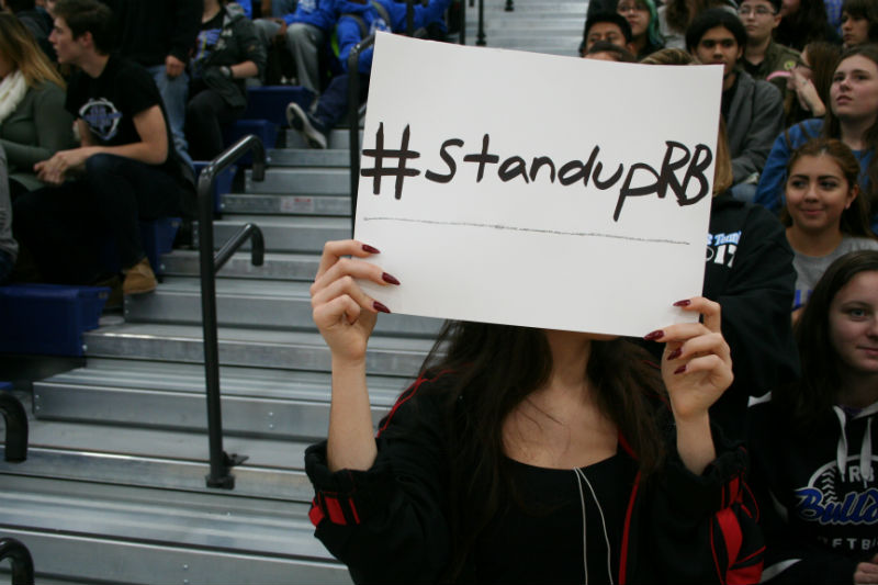 A student holds up a #StandUpRB sign in solidarity with the recent protests at the Pride and Positivity Assembly.